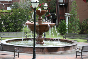 A park water fountain, a light post and two benches.